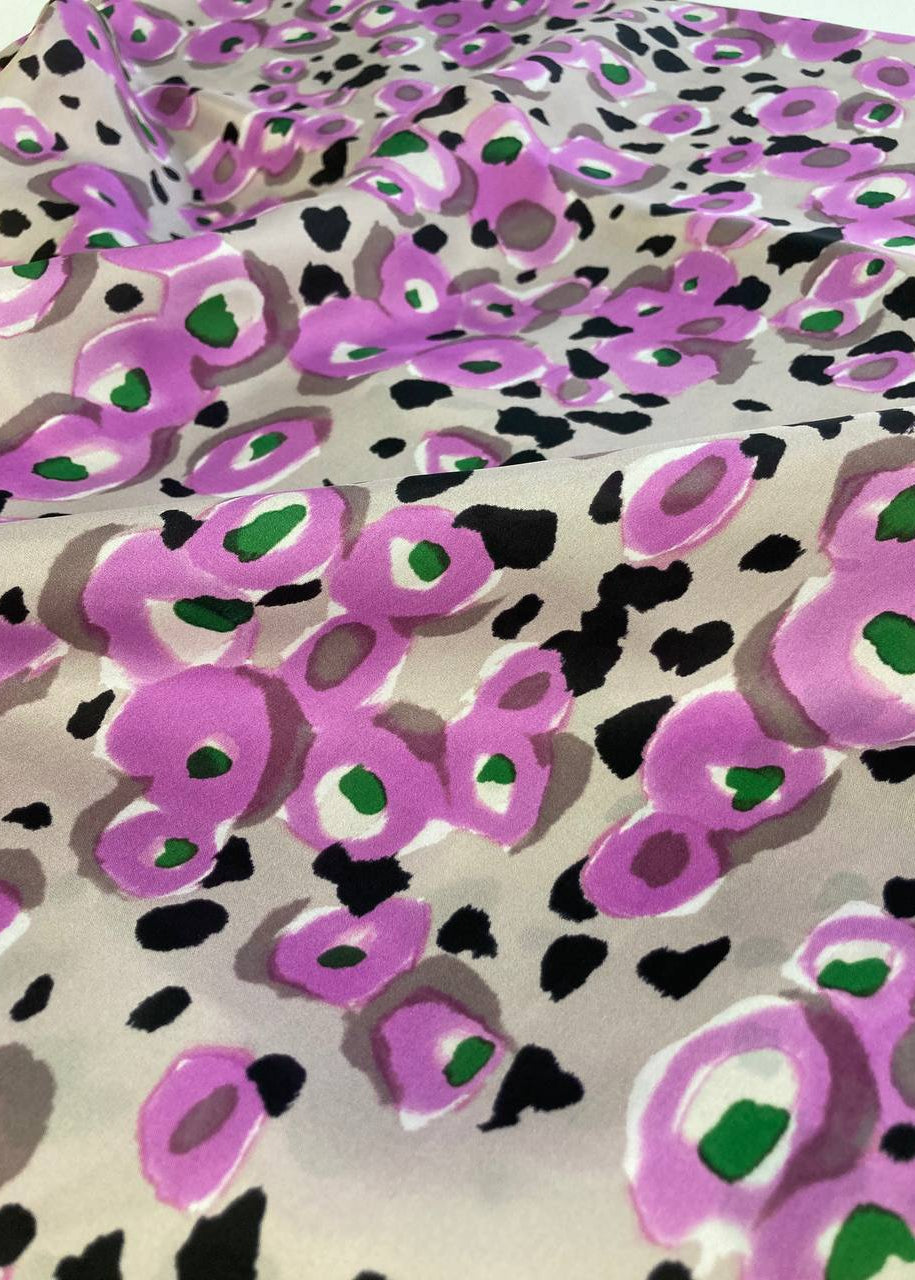 Fabric with a leopard print pattern featuring purple, black, and green colors on a beige background.