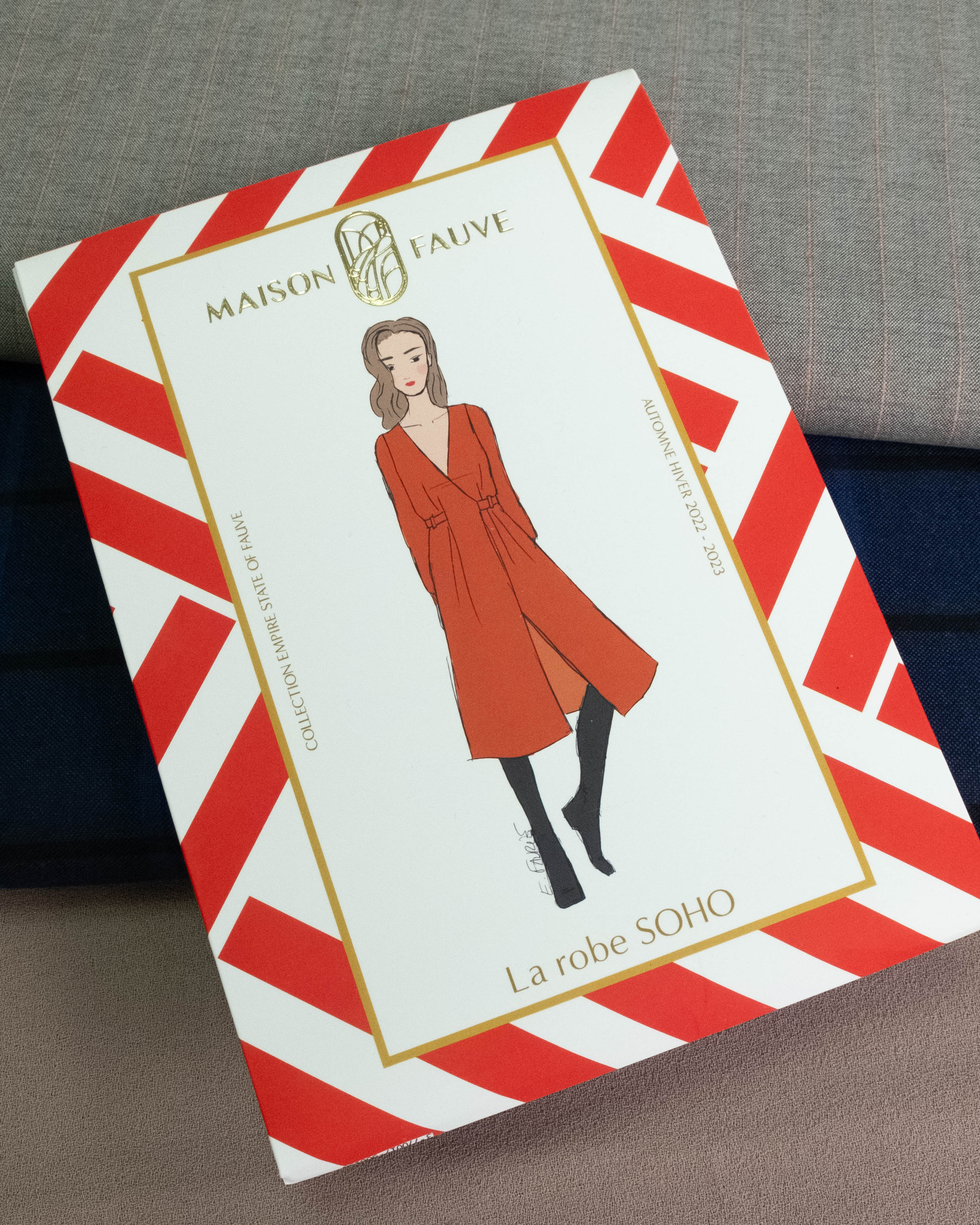 Maison La Auve 'La robe SOHO' pattern box featuring a red illustrated dress on a white background with red and white diagonal stripes, placed on a gray fabric surface.