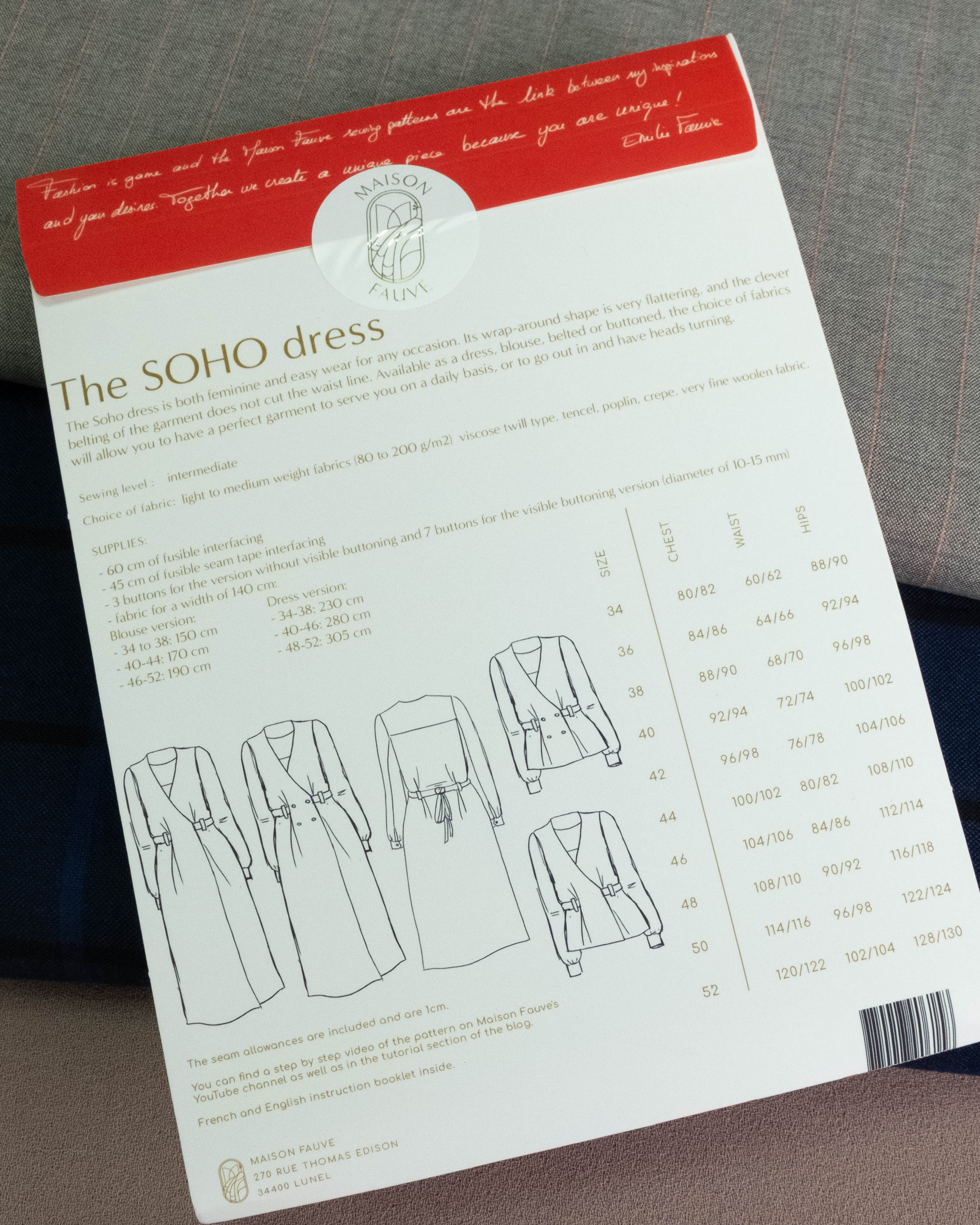 A sewing pattern sheet for 'The SOHO dress' by Sakai Sewing Machines, showing line drawings of the dress design and sizing tables, photographed on a gray fabric surface.