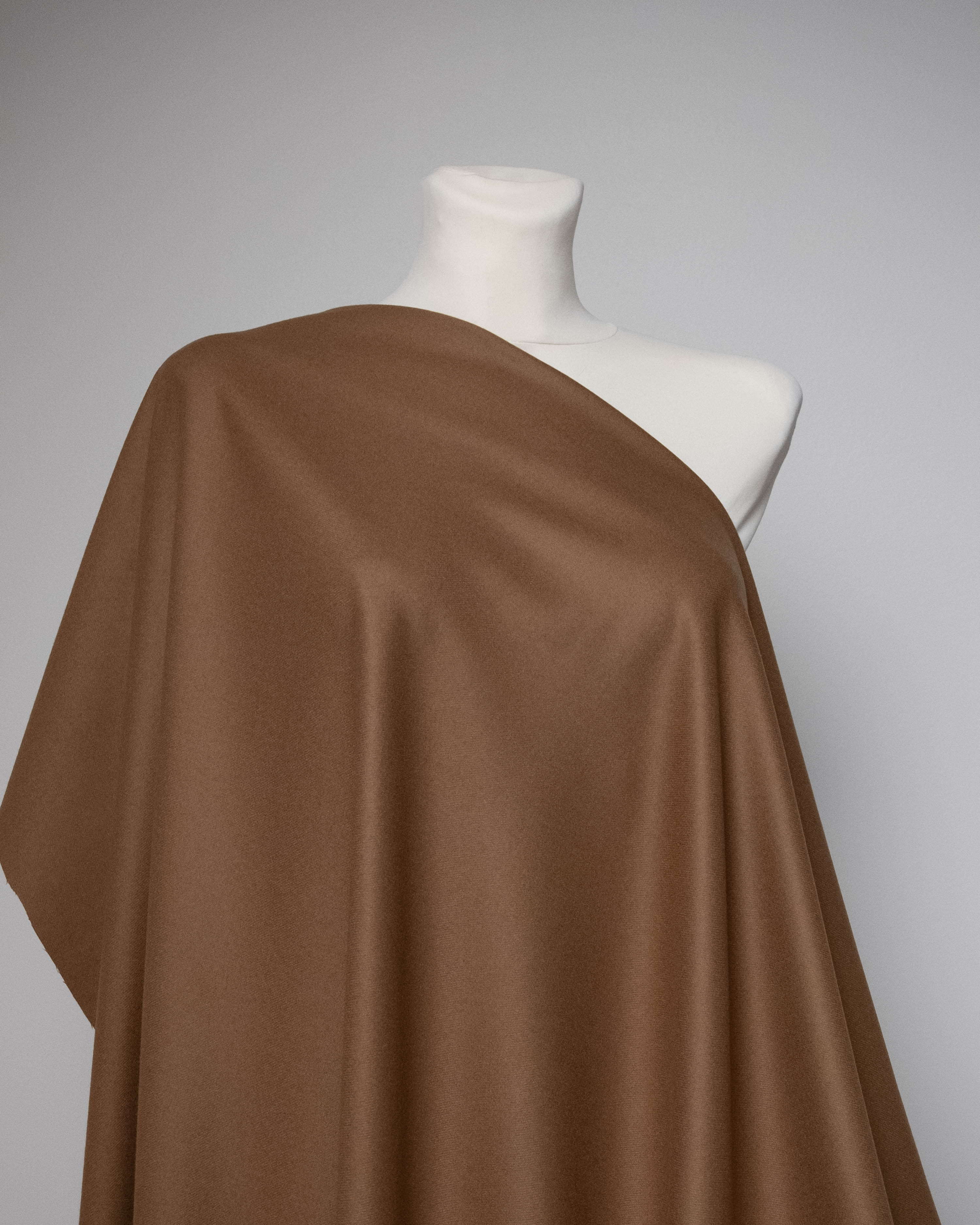 A draped brown fabric, likely satin or silk, displayed on a white mannequin torso against a neutral gray background.