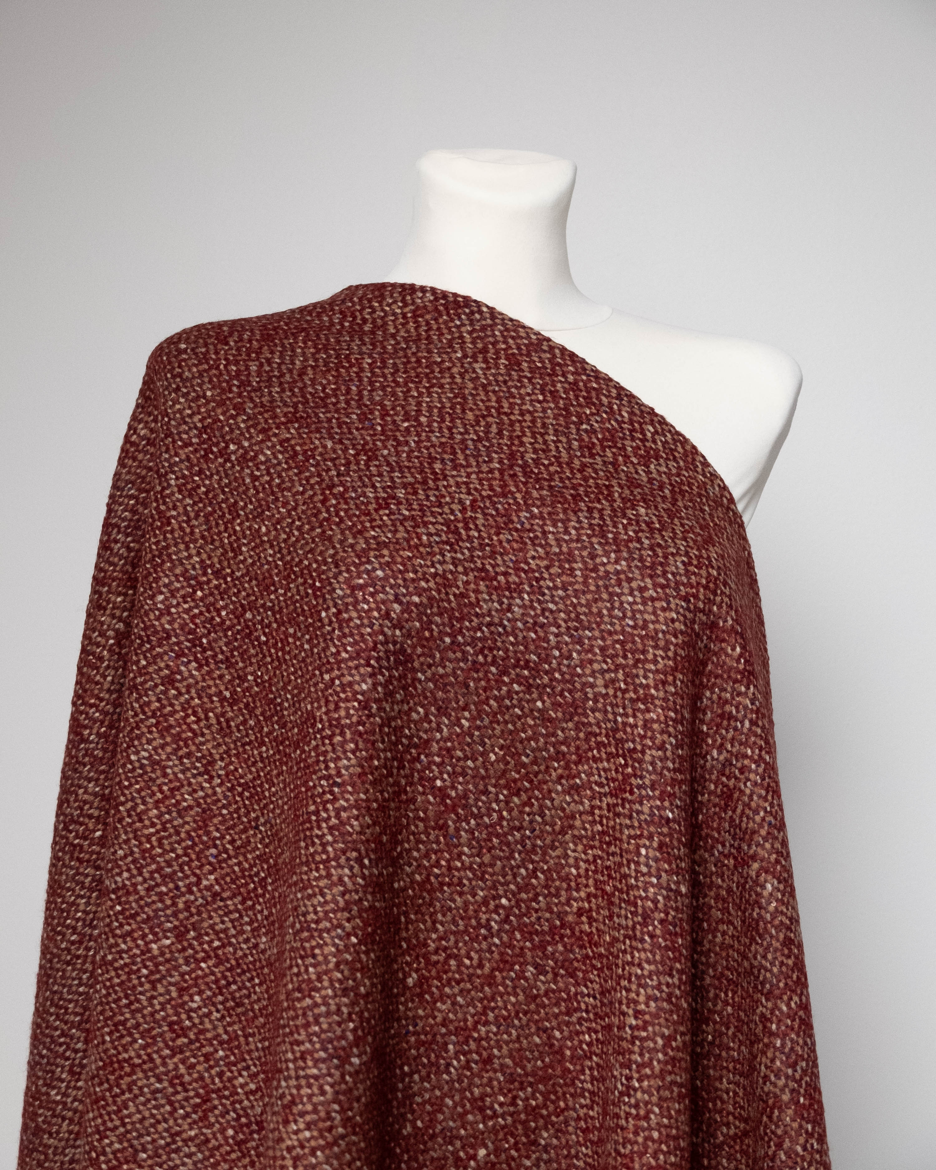 A textured, heathered rust-red or burgundy knit shawl draped over a white mannequin torso against a light gray background.