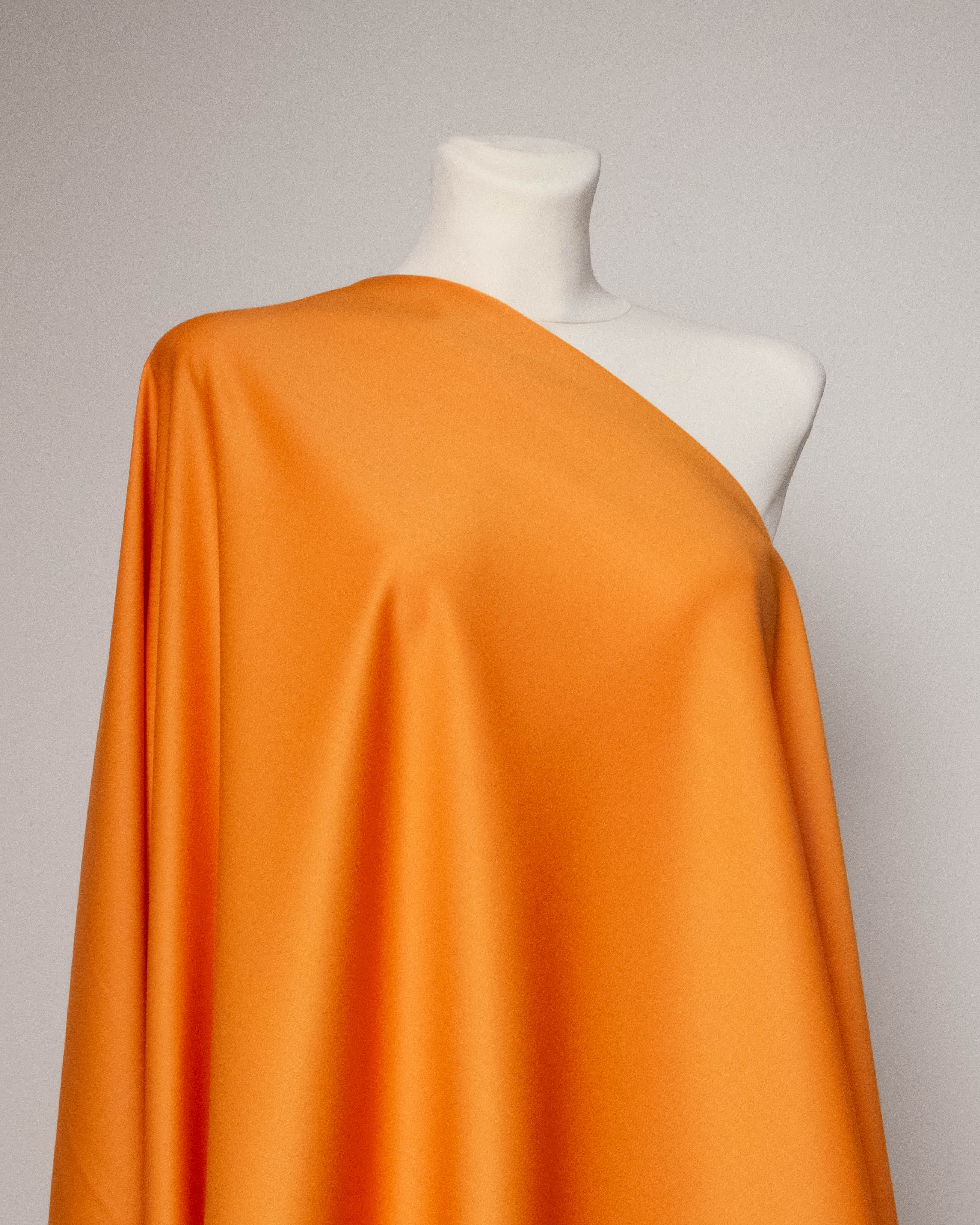 Bright orange draped fabric displayed on a white mannequin torso against a light gray studio background.