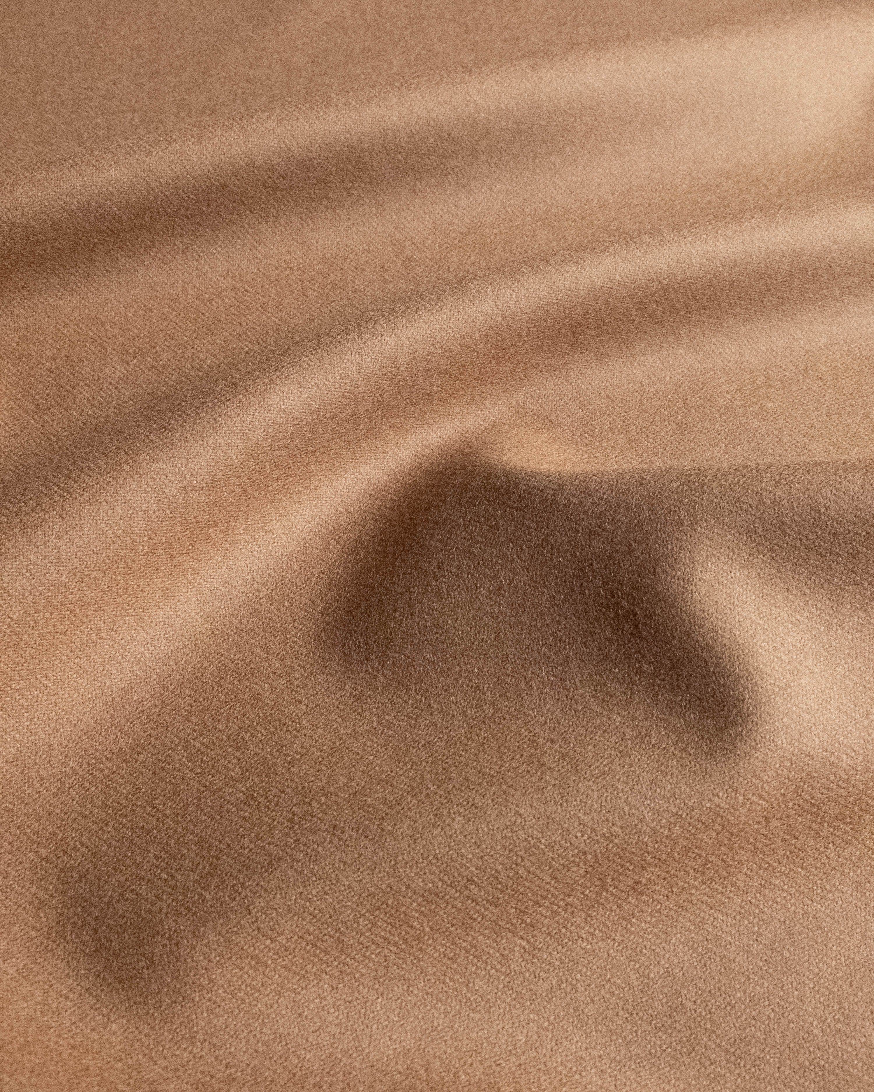 A close-up of draped tan fabric with soft folds and a smooth texture.