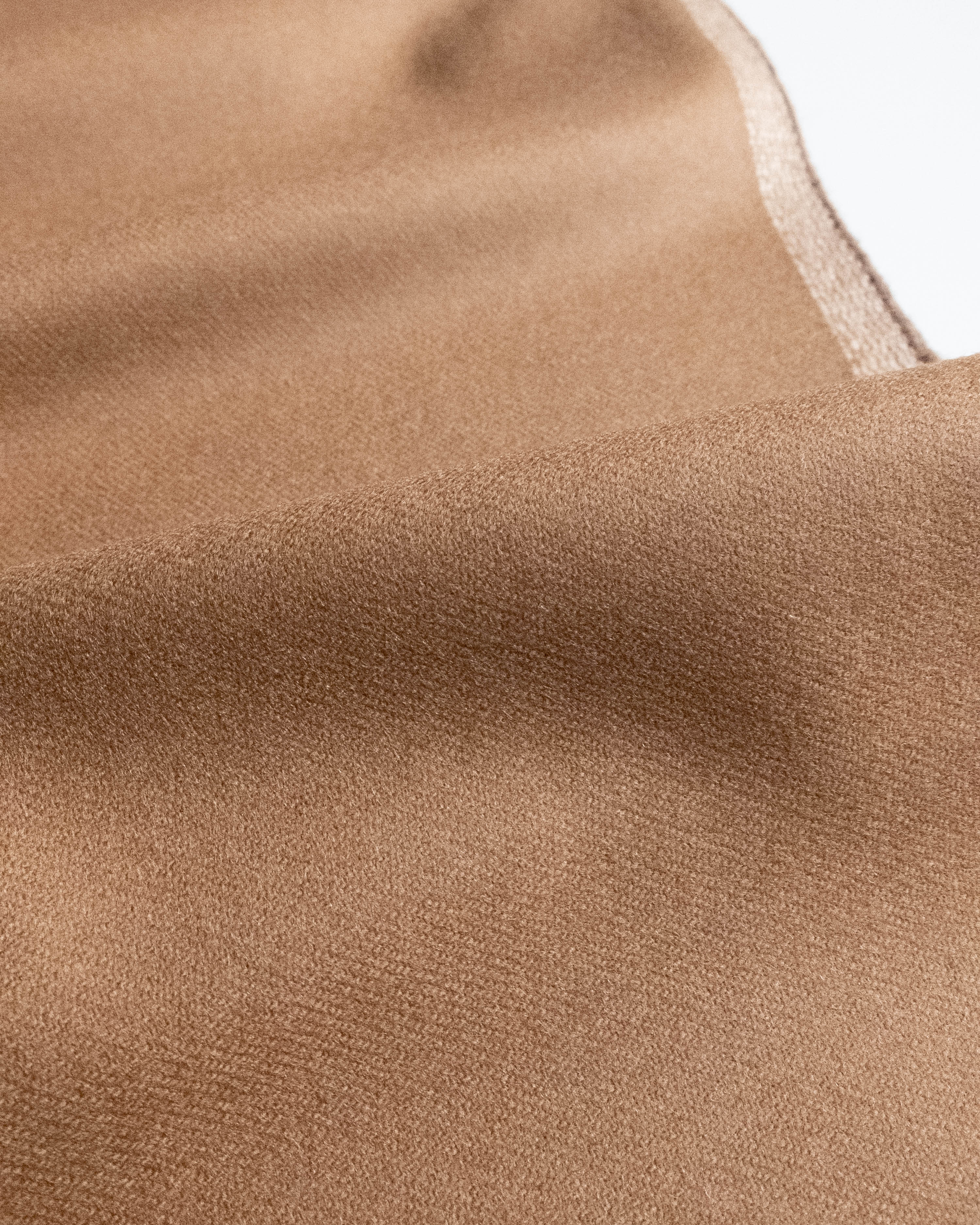 A close-up of a soft, draped fabric in a warm camel brown color, showing its fine texture and a subtle lighter edge.