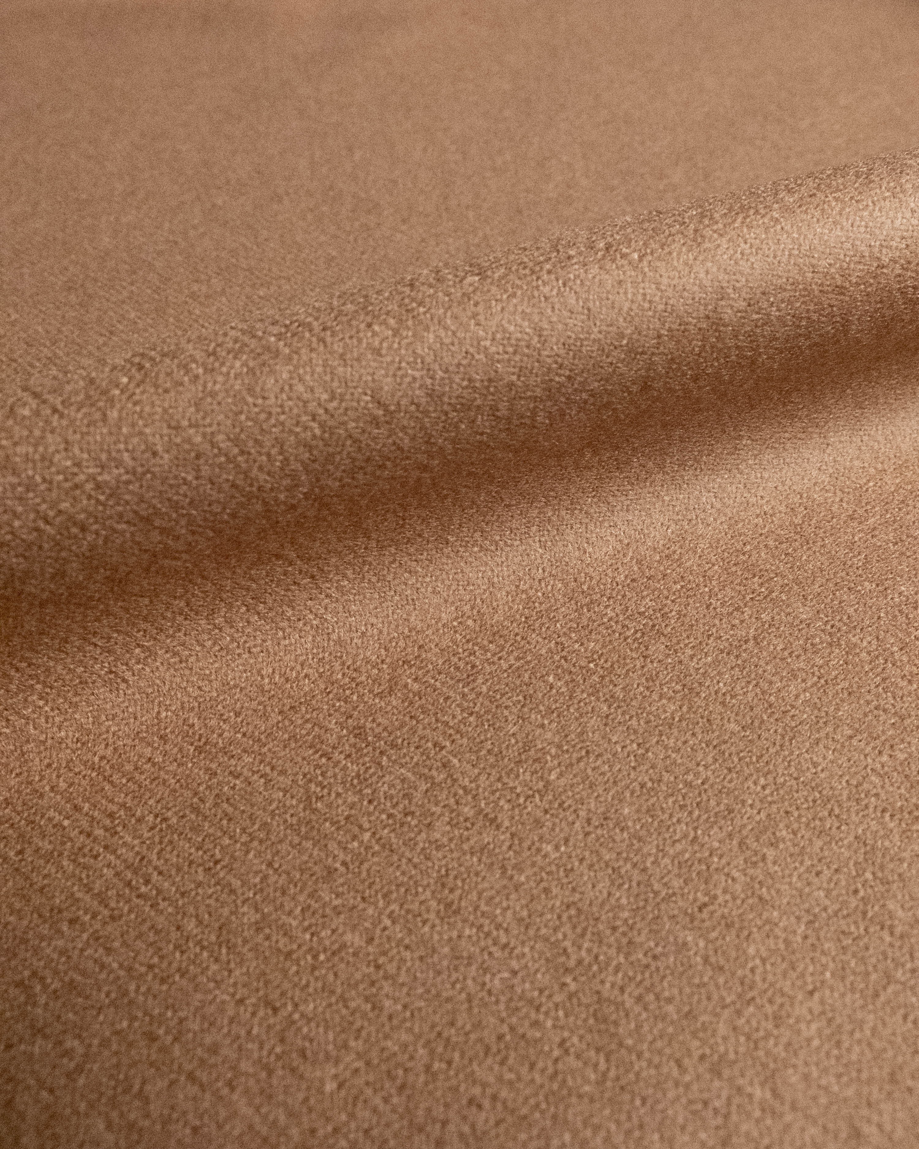 A close-up of a soft, textured fabric in a warm camel brown color, showing its fine woven texture and gentle folds.
