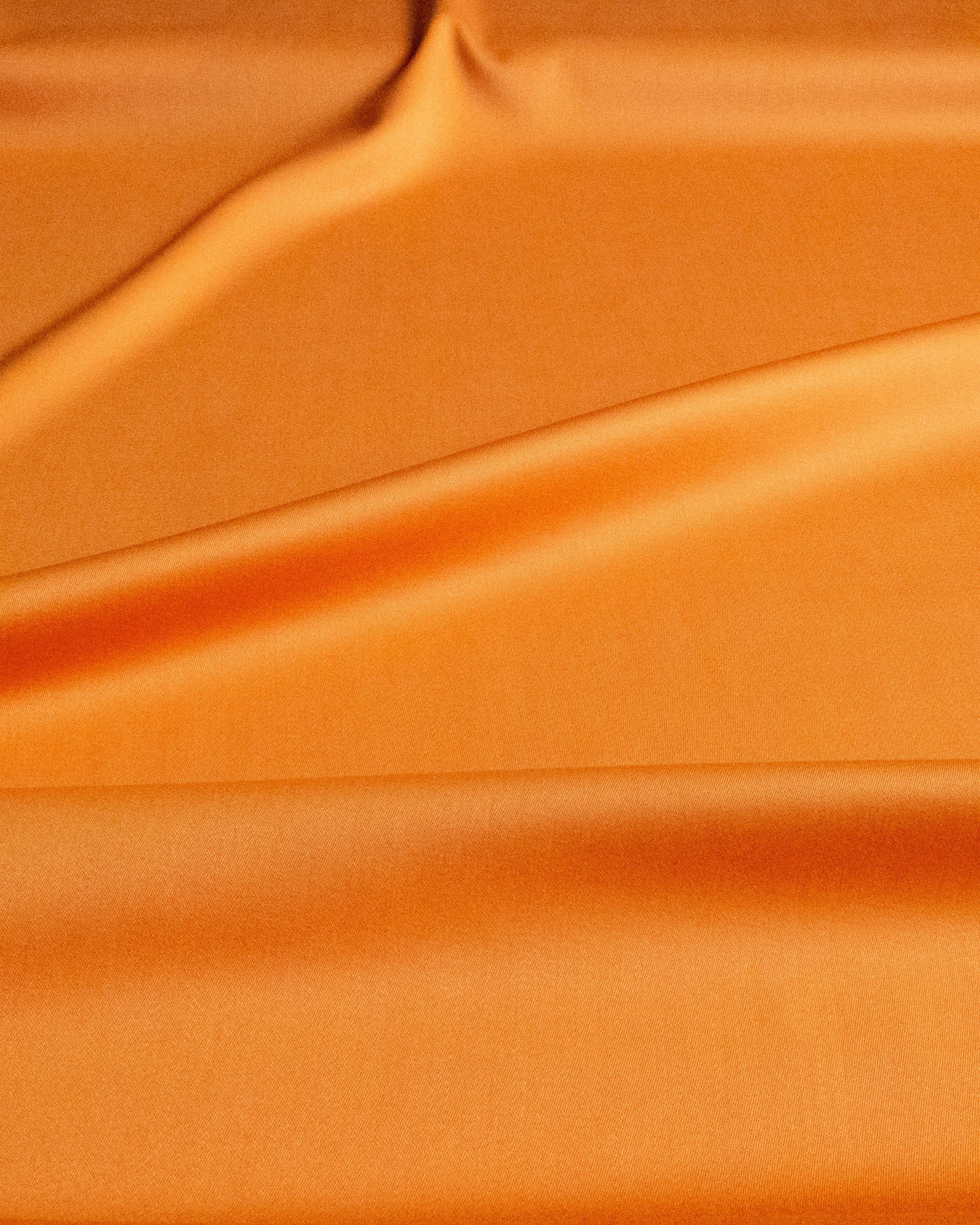 A close-up of draped orange satin fabric with soft folds and a smooth, glossy texture.