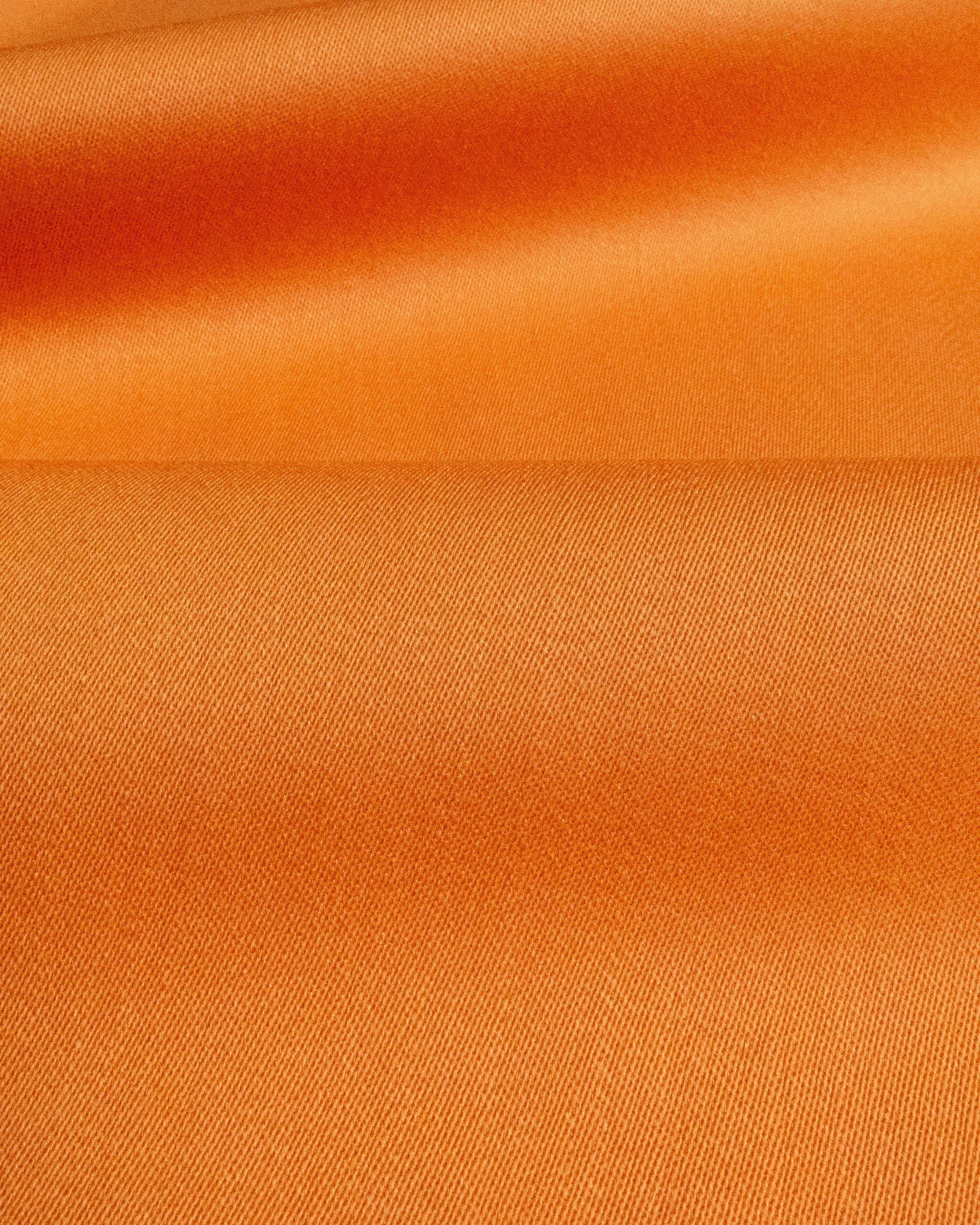 A close-up of smooth orange fabric with soft folds and a fine woven texture.