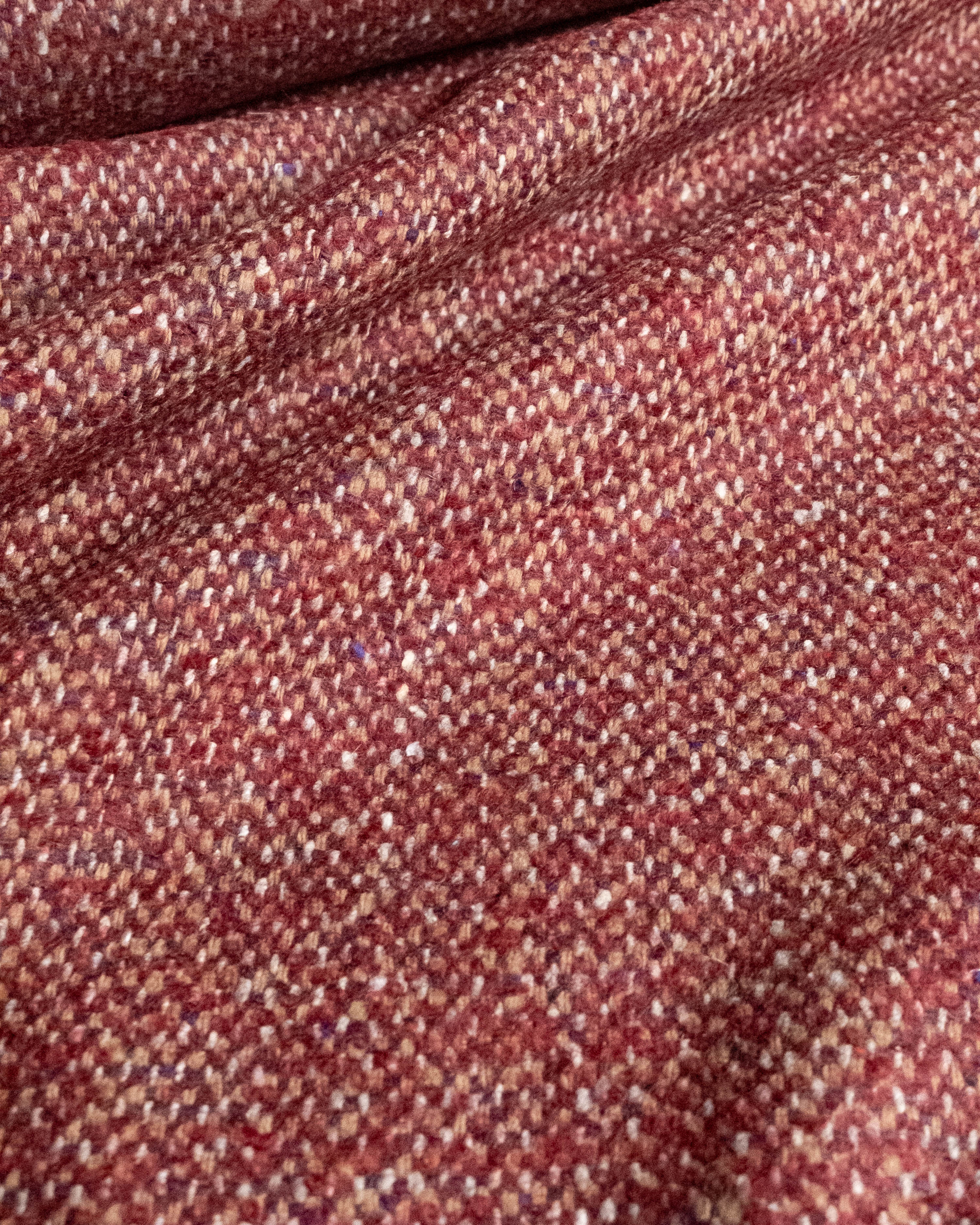 A close-up of a textured woven fabric in a heathered rust red and beige colorway, showing the detailed tweed-like weave and soft folds.