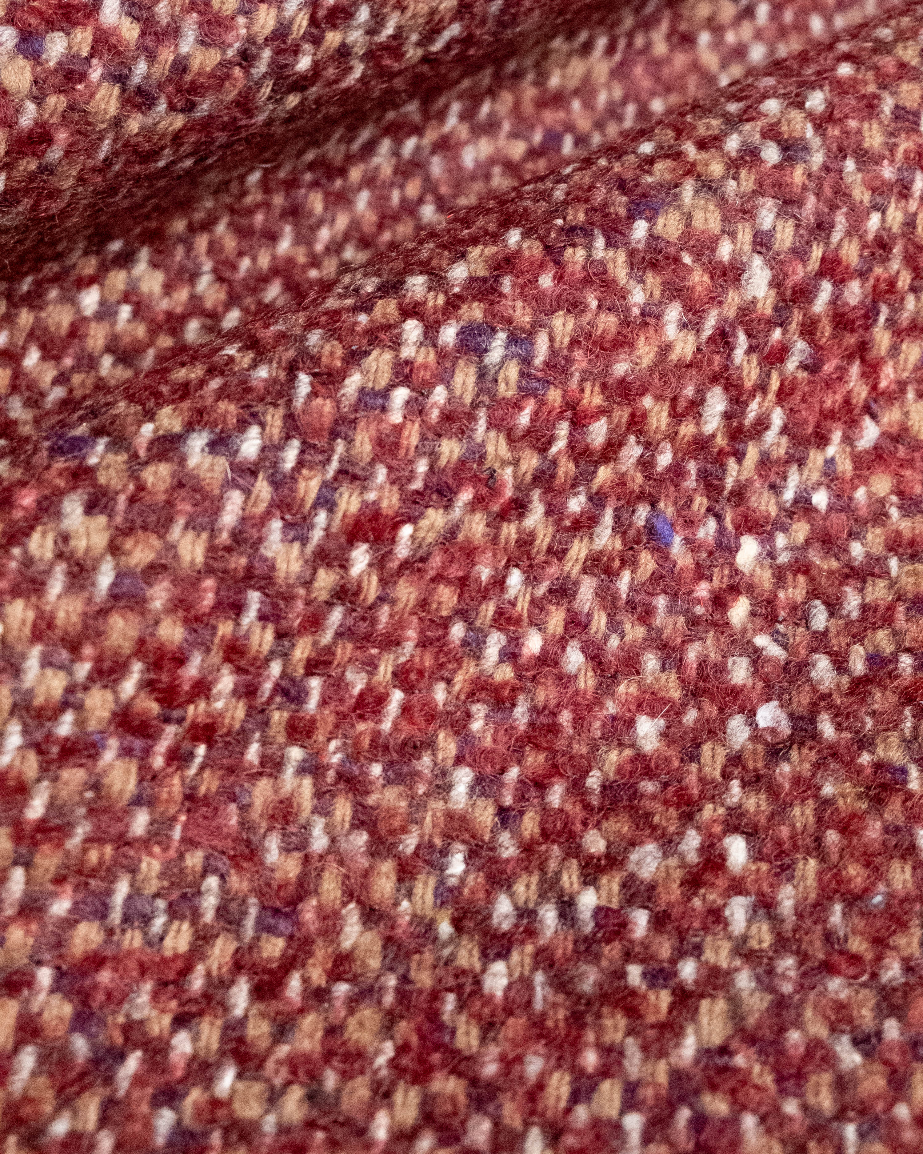 A close-up of a textured woven fabric with a heathered pattern of rust red, brown, beige, and white threads.