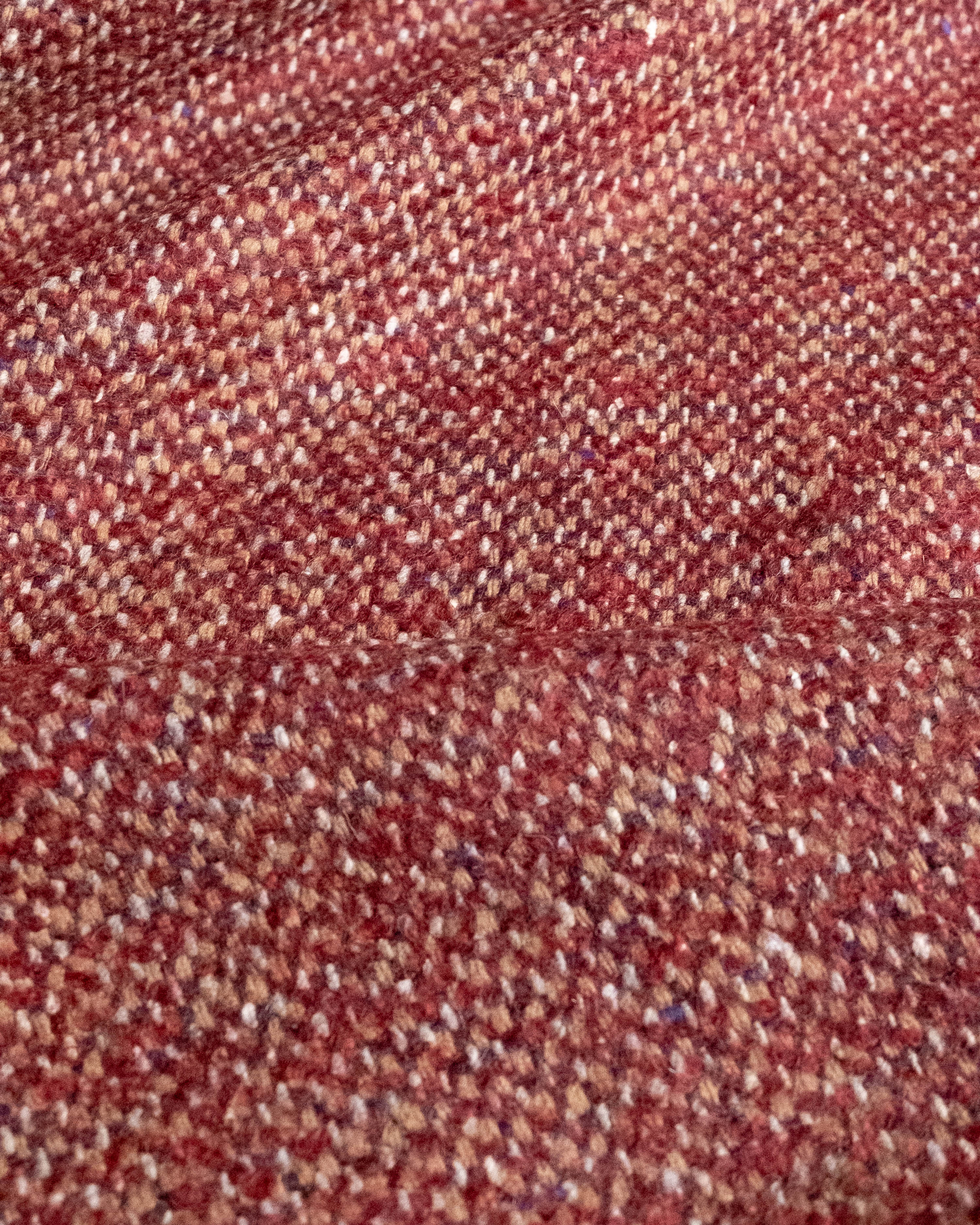 A close-up of a woven fabric texture in a heathered red and beige tweed pattern.