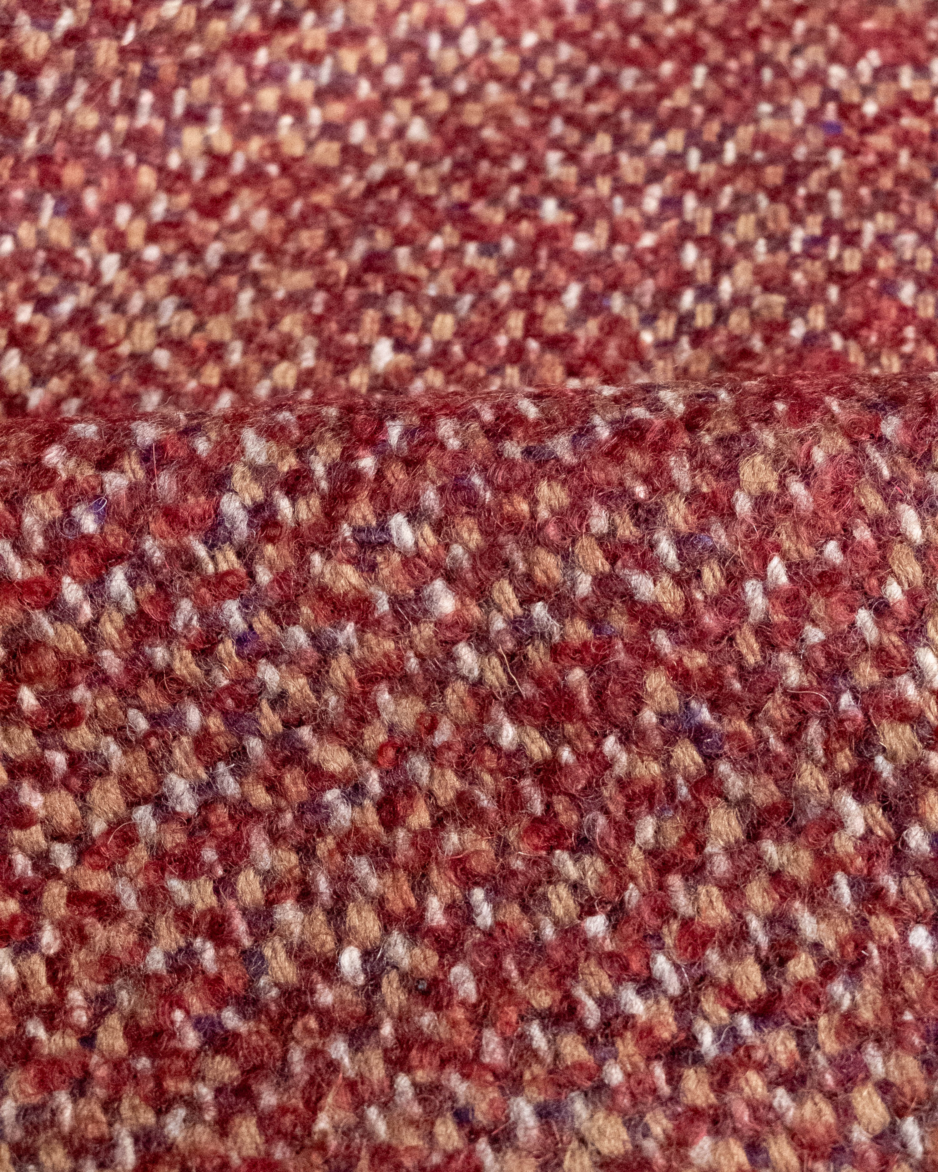 A close-up of a textured woven fabric with a heathered pattern in red, brown, beige, and white threads.