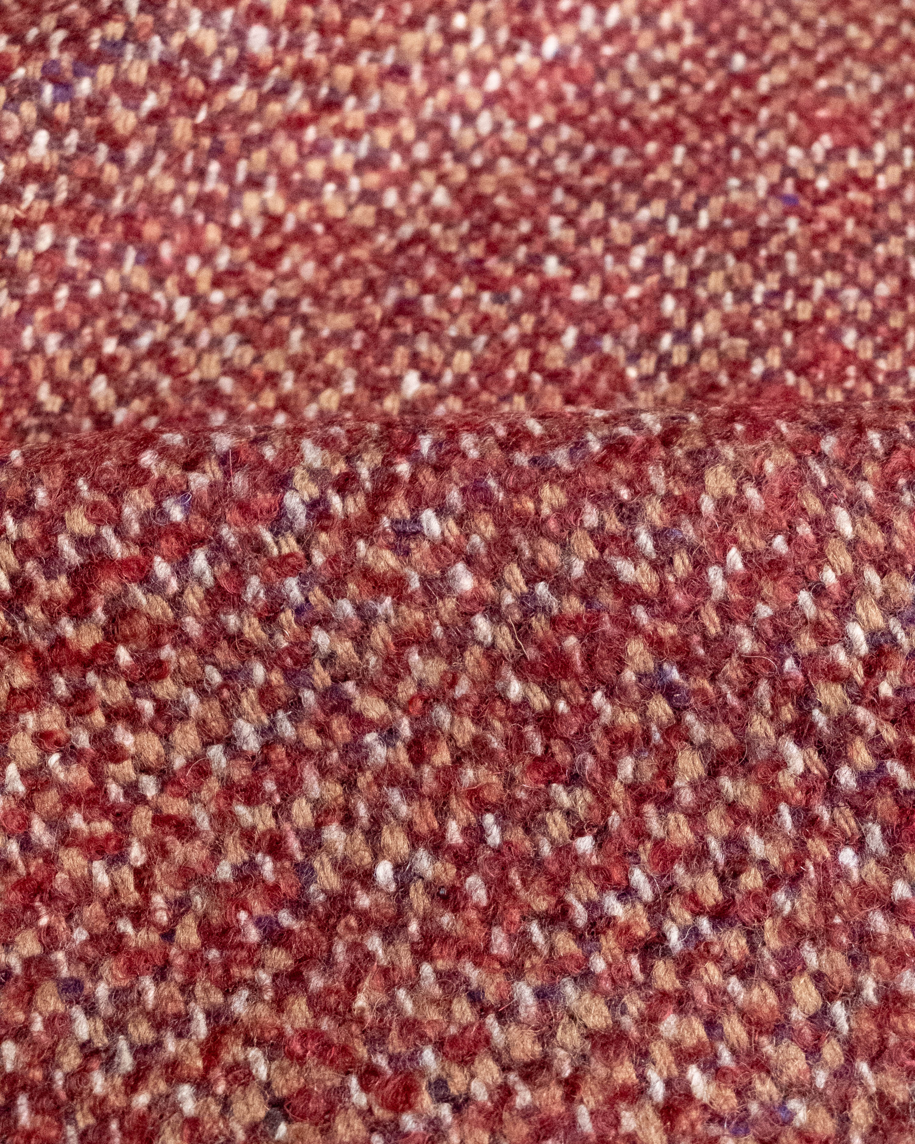 A close-up of a woven fabric texture in a heathered mix of rust red, brown, beige, and muted purple threads.