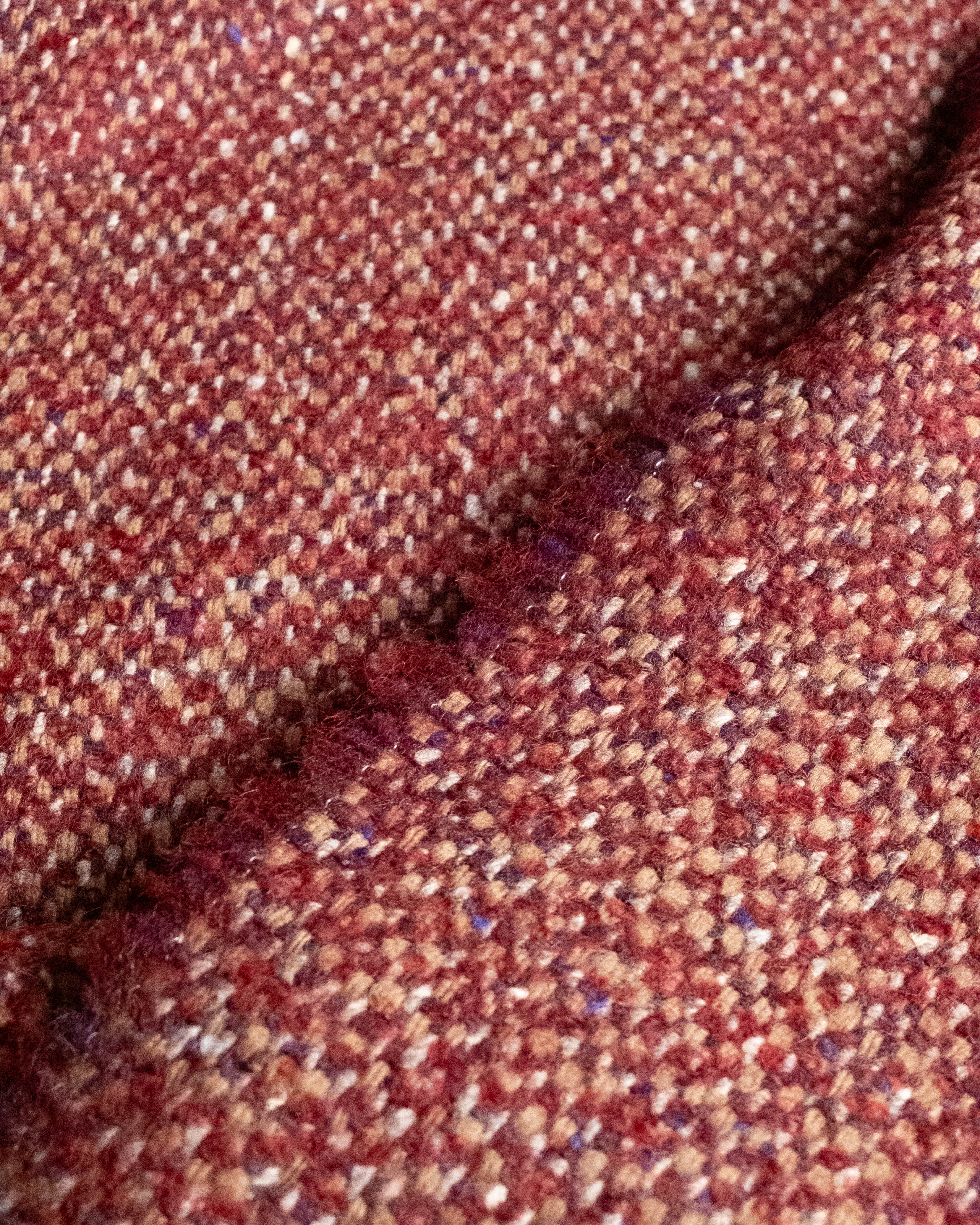 A close-up of a textured tweed fabric in a heathered mix of rust red, brown, and beige threads, folded to show the weave detail.