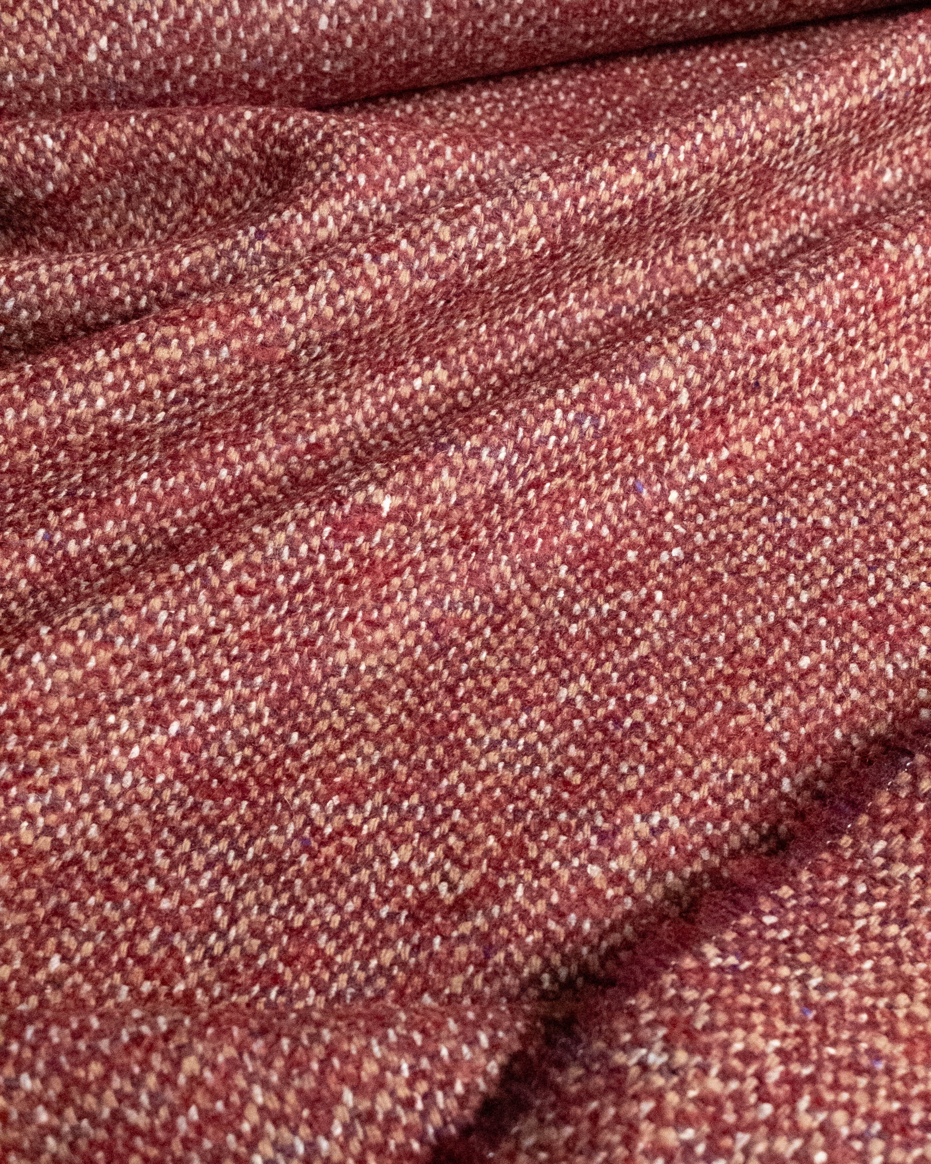 A close-up of a textured woven fabric in a heathered rust red and beige colorway, showing the detailed tweed-like weave and soft folds.