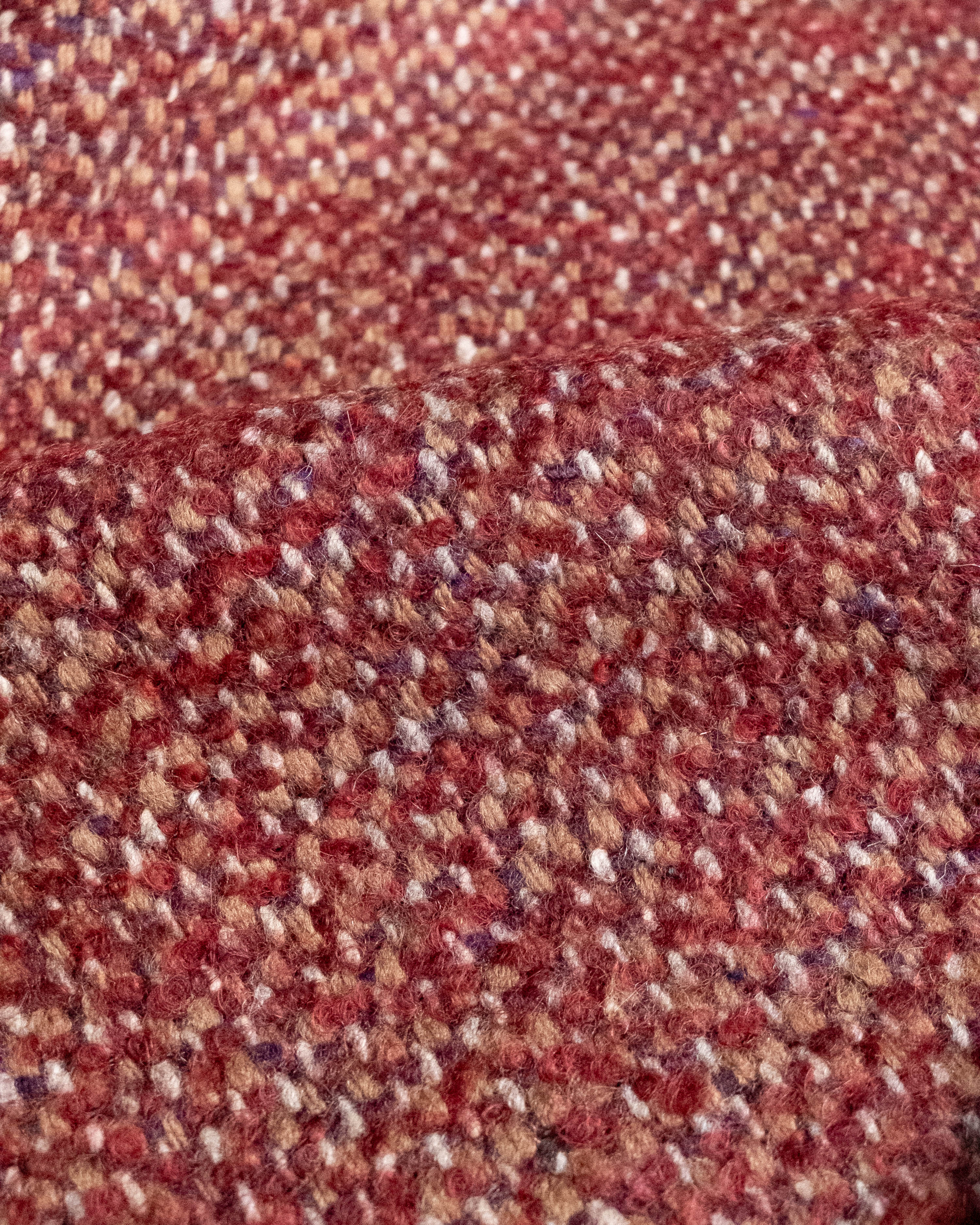 A close-up of a textured woven fabric with a heathered pattern in rust red, brown, beige, and white.