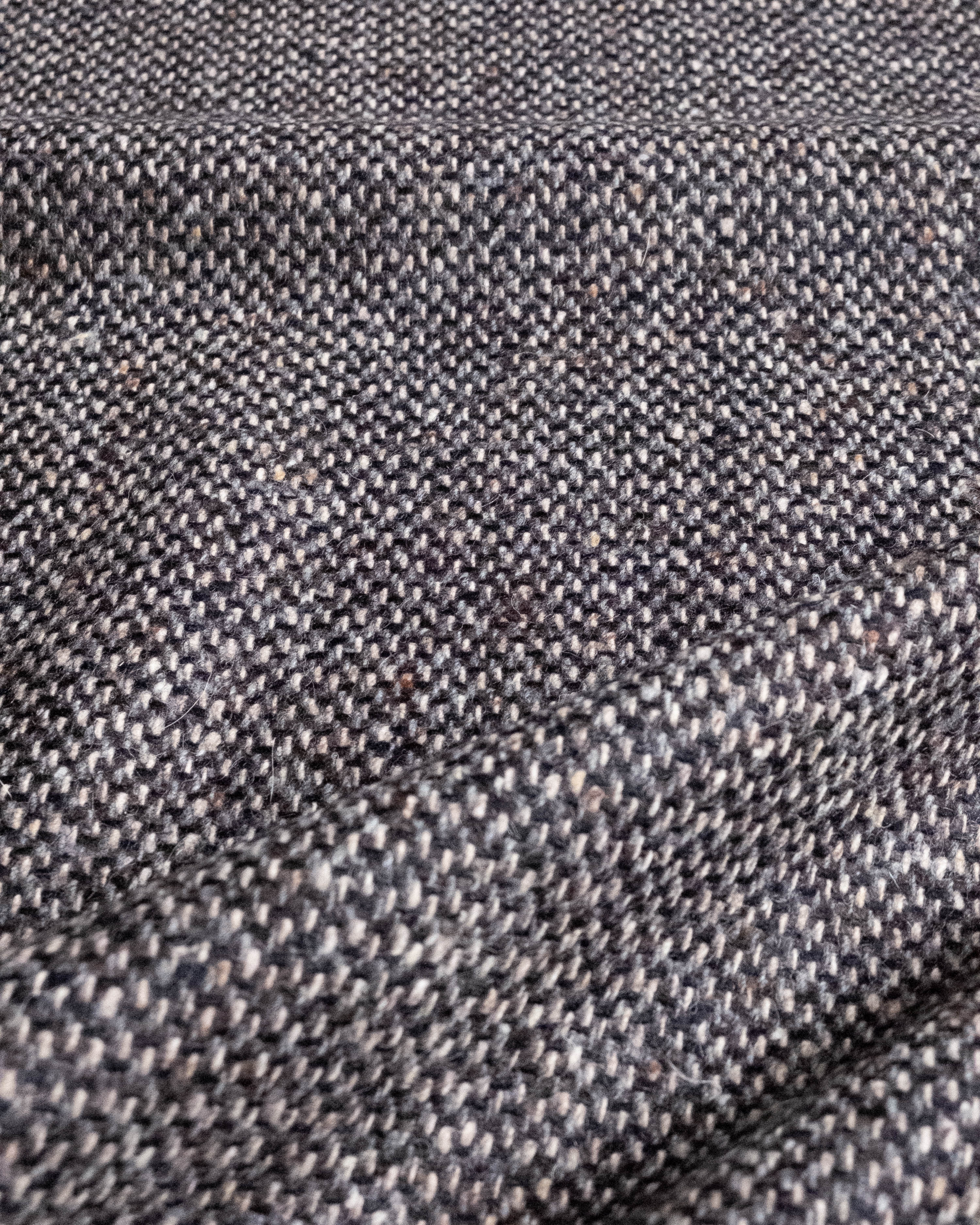 A close-up of a textured woven fabric with a herringbone pattern in dark gray, charcoal, and black.