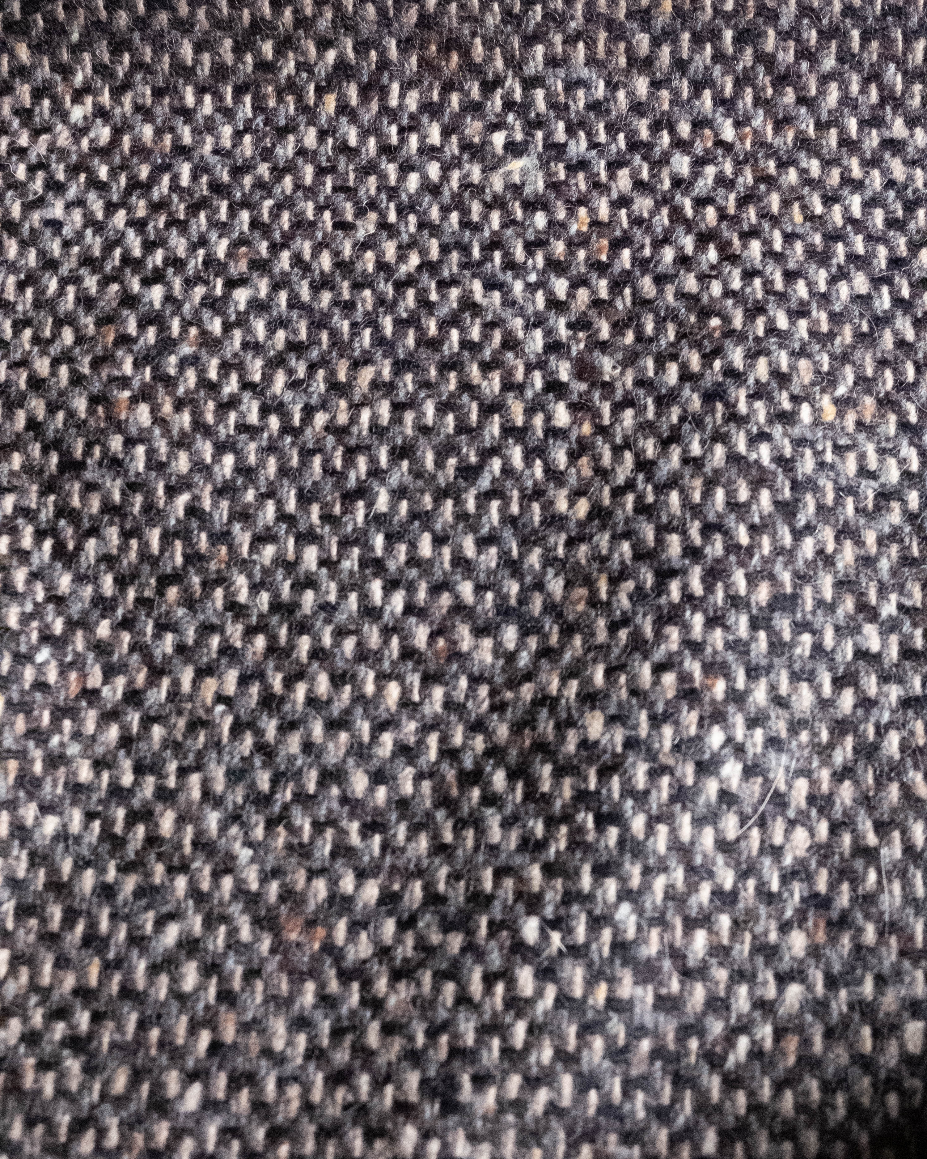 Close-up of a textured woven fabric with a dark charcoal gray and beige herringbone pattern.