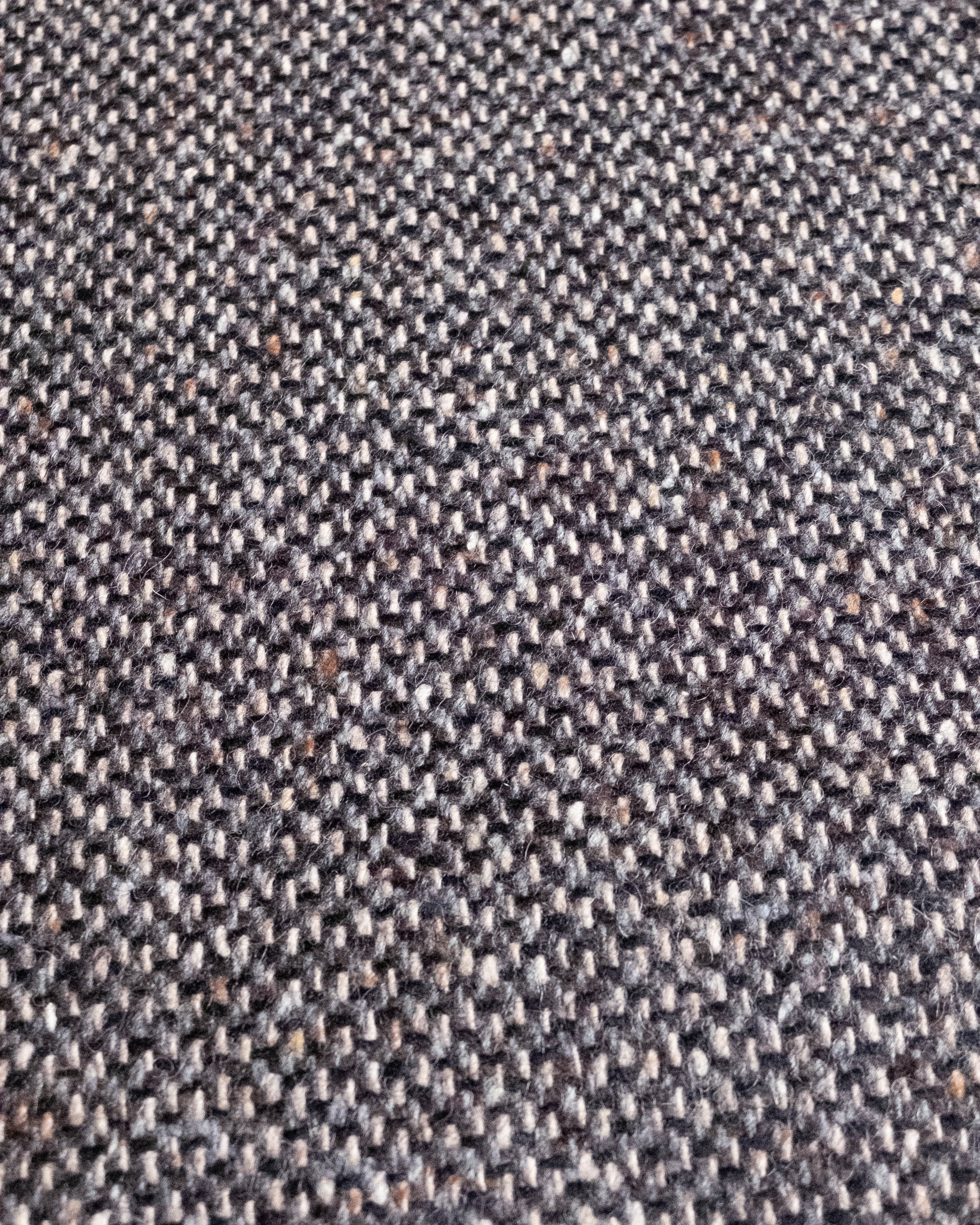 A close-up of a woven fabric texture with a dark gray and beige herringbone pattern.
