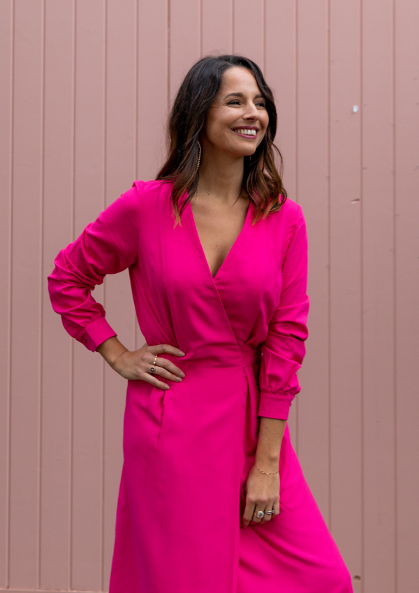 Woman wearing a bright pink dress standing against a pink wall.